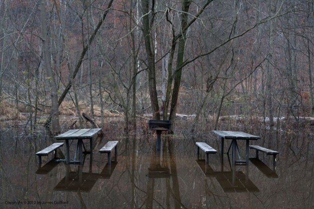 Photo: Picnic tables in a park are reflected in shallow flood waters. Photo by James Guilford.