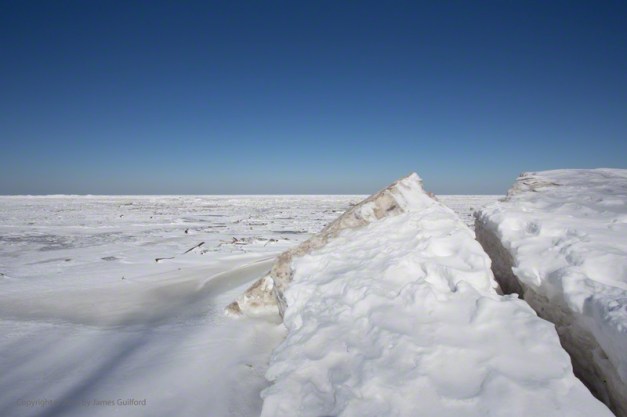 Photo: Piles of broken ice plates rest deep over a Lake Erie beach under a clear winter sky. Photo by James Guilford.