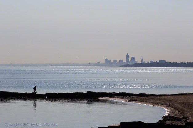 Photo: Woman stepping on stones of breakwall with city in background. Photo by James Guilford.