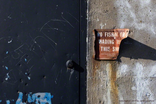 Photo: Damaged door and sign on concrete wall. Photo by James Guilford.
