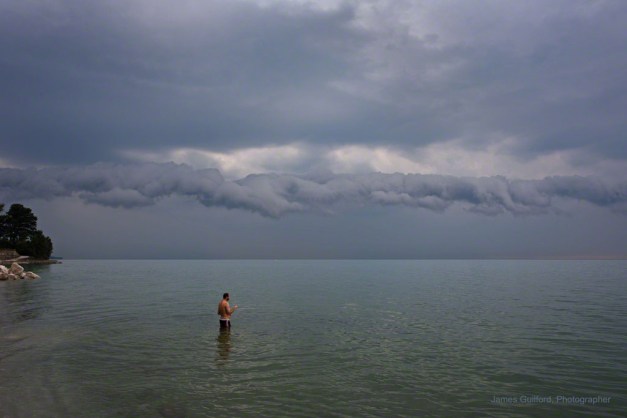 Photo: Man wading in lake as a storm approaches. Photo by James Guilford.