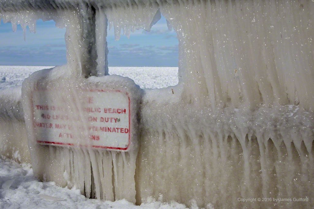 Photo: Guardrail and sign covered in thick curtains of lake water ice. Photo by James Guilford.