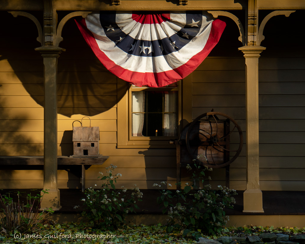 Photo: Times Remembered. Rustic items sit on a porch under patriotic bunting lit by late-day sun. Photo by James Guilford
