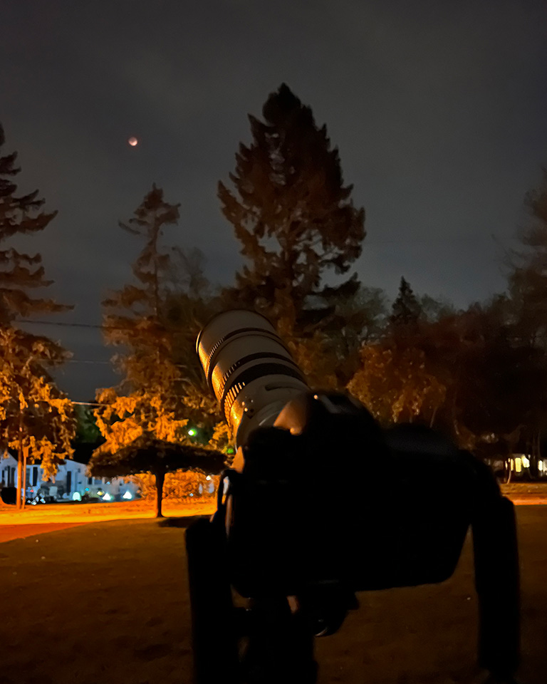 Camera rig used to make lunar eclipse photos -- camera with telephoto lens aimed at eclipse, visible in cloudy sky.