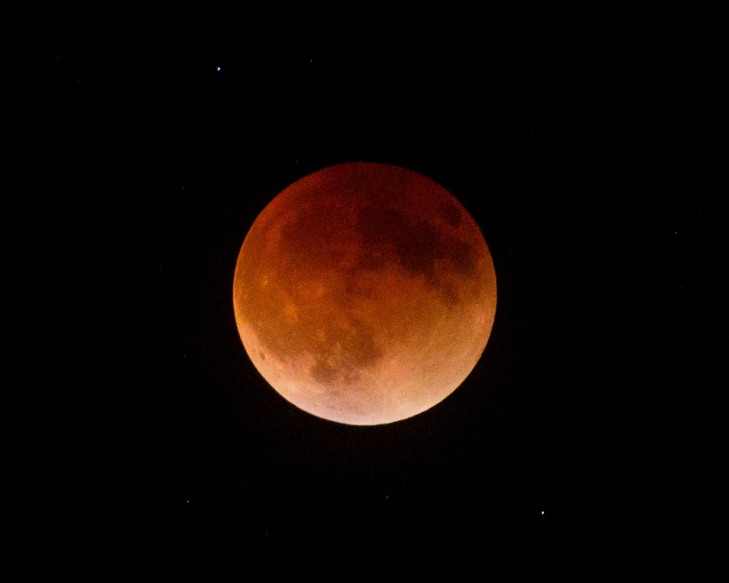 Deep red and copper tones mark totality. No direct light from Sun reaches Moon during this period leaving only light scattered and filtered through Earth's atmosphere -- coloration from all of Earth's sunrises and sunsets -- to make Moon visible. The two bright dots in the blackness are stars in constellation Libra. Total Lunar Eclipse of May 15 - 16, 2022, at 12:31 a.m. EDT. Camera Info: Canon EOS 5D Mk. 4, 400mm lens, ISO 8000, f/5.6, 1/4-second. Photo by James Guilford.