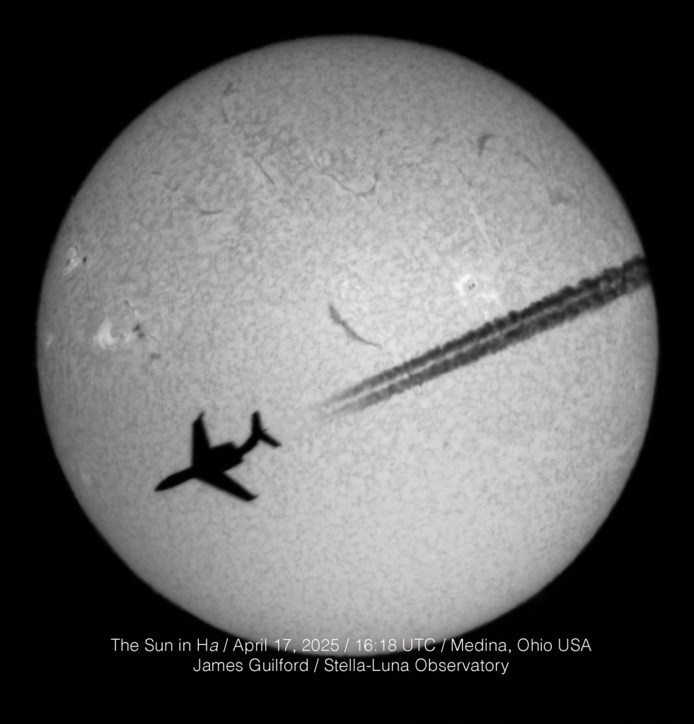 A business-class jet is seen in silhouette, streaming contrails, as it crosses the disk of the sun. The solar disk is mottled with sunspots, and filaments scattered across its surface -- mostly in the upper or northern hemisphere.